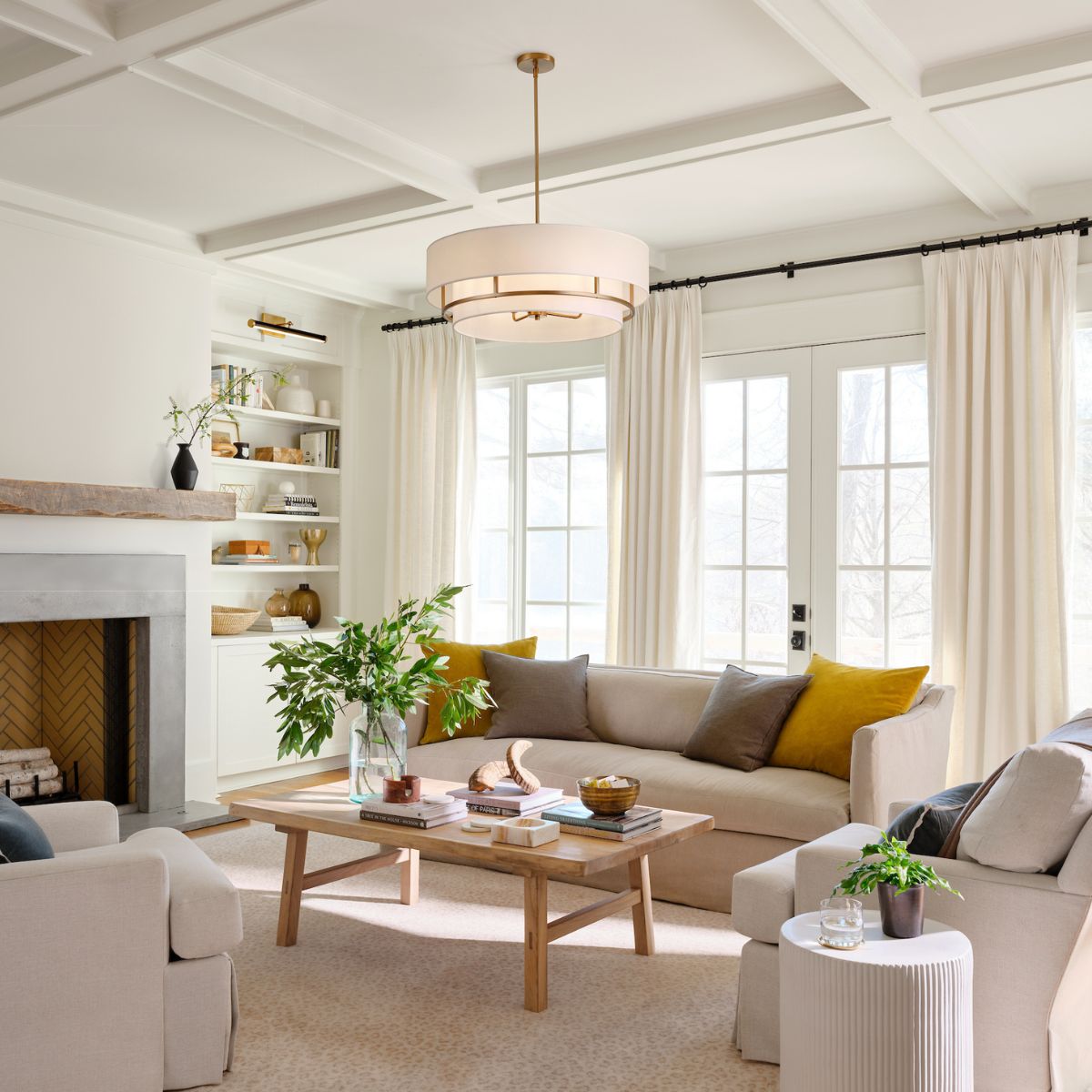 A bright, airy living room with a white coffered ceiling, a large drum pendant light, a neutral sectional sofa, and a light wood coffee table.