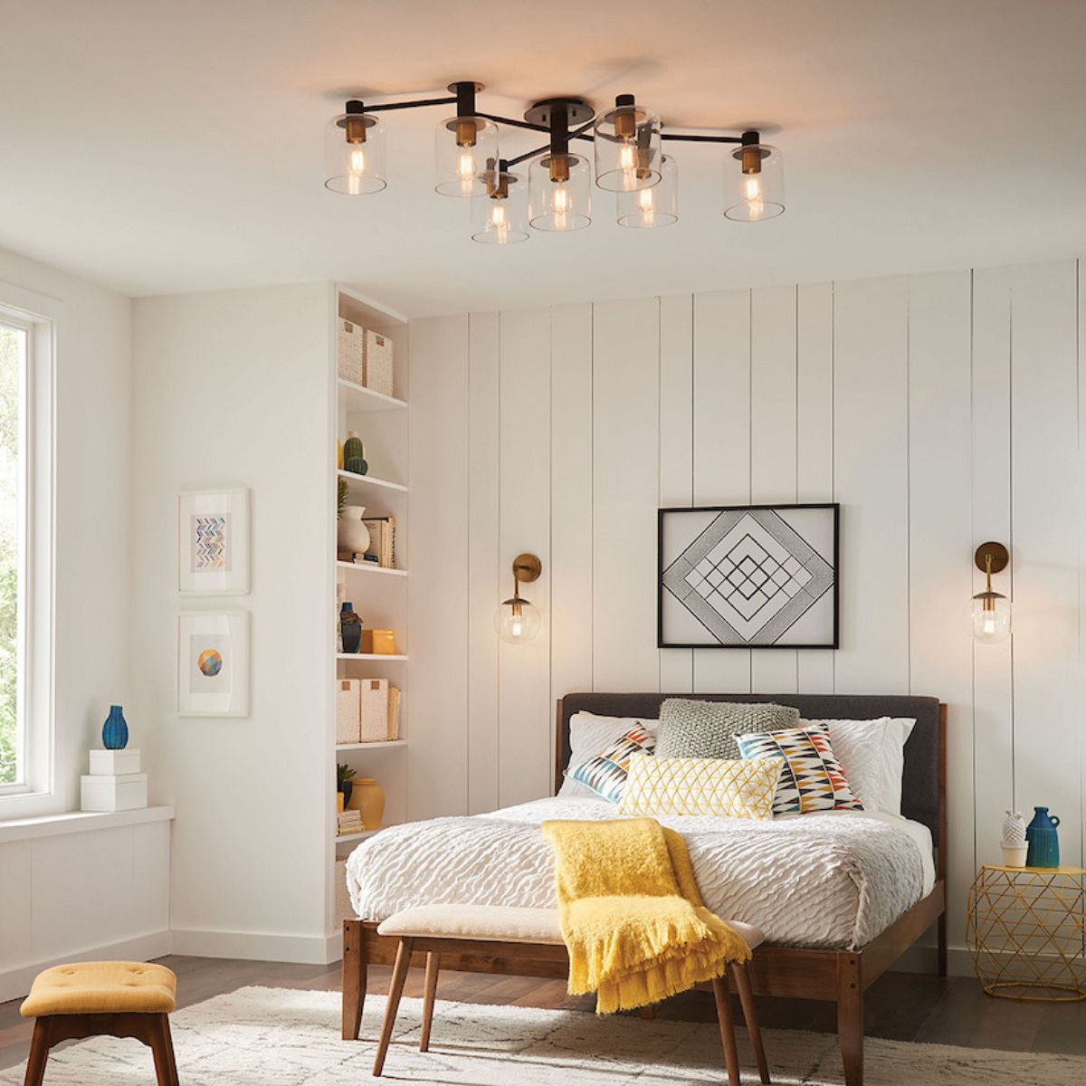 A modern bedroom featuring a black multi-bulb sputnik ceiling light, white vertical shiplap walls, and a mid-century modern bed with yellow and grey accents.